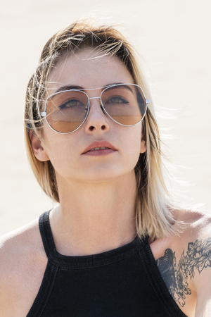Portrait of a beautiful woman with a tattoo in a T-shirt and sunglasses, close-upの写真素材