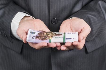 bundle of money in denominations of five hundred euros and eurocents on it in the hands of a businessman in a suitの写真素材