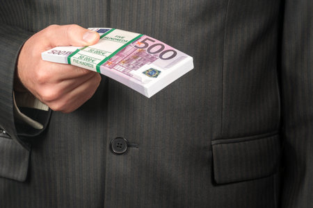businessman in suit holding a bundle of money with a face value of five hundred euro, closeup