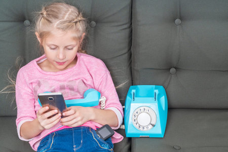 child uses a smartphone while holding the handset from the phone in your hand and retro old phone in...