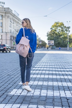 woman looking back goes on a pedestrian crossing on the pavement, rear viewの写真素材