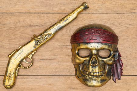 pirate mask in the shape of a skull and a vintage pistol lying on a wooden tableの写真素材