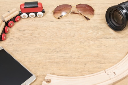smartphone, sunglasses, toy train and lens on an old wooden table as a travel conceptの写真素材