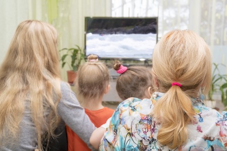 Grandmother, daughter and granddaughters watching television, back view, blurred backgroundの写真素材