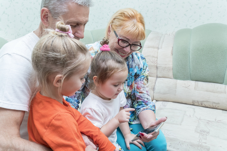 grandparents and grandchildren with a smile look at the phone while sitting on the couchの写真素材