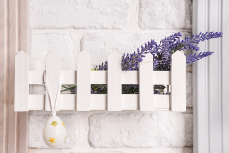 Easter egg hanging on a decorative shelf - a fence on a white brick wallの写真素材
