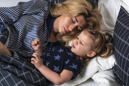 Mother and daughter lie in bed in the evening and daughter pretends to be asleepの写真素材