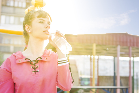 beautiful sporty woman drinks water from a bottle against the sunの写真素材