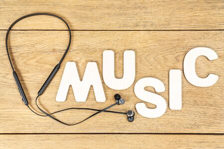 word music laid out of wooden letters next to wireless headphones on an old wooden tableの写真素材