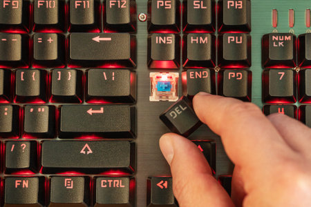 male hand holds delete button over broken red backlit keyboard