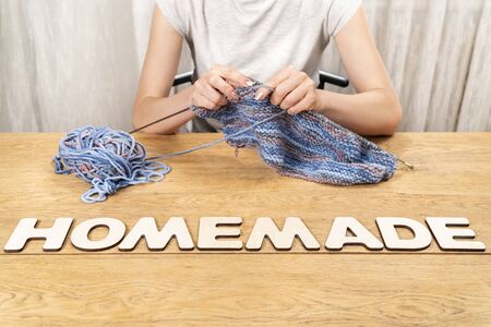 word homemade is laid out in wooden letters on an old wooden table where a woman knitsの写真素材