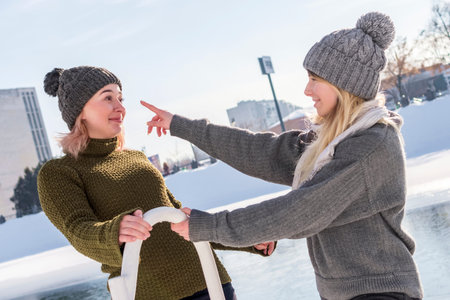 one woman tries to touch her friend nose while standing by the river in winter