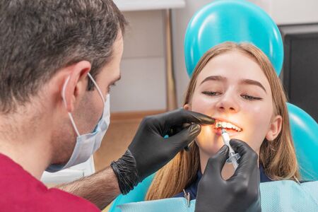 doctor applies a blue medicine to the patient tooth with a syringeの写真素材