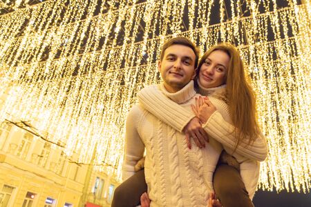 woman climbed onto the back of the man on a background of festive lights at nightの写真素材