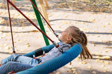 Little cheerful girl swinging on a swing - basket