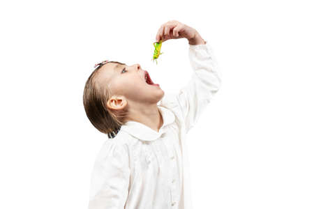 little beautiful girl opened her mouth to eat a green grasshopper isolated on white backgroundの写真素材