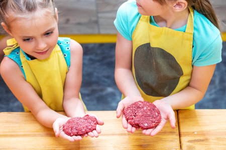 children in aprons make patties of minced meat on a wooden tableの写真素材