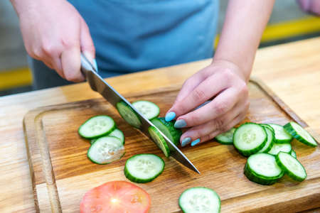 female hands cut cucumber into slices on a wooden cutting boardの写真素材
