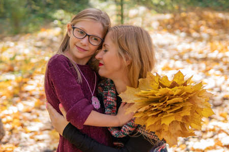 Mother lovingly hugs her daughter, with a bouquet of yellow autumn leaves in her handの写真素材