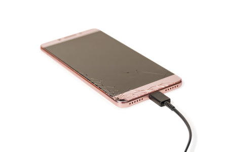 smartphone with broken screen charging via cable isolated on white background