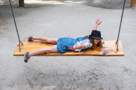girl in a hat is rolling on a bench - a swing, arms outstretched, copying the plane or bird