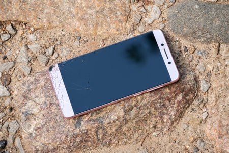 pink new phone with broken screen lies on rocks