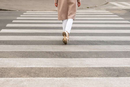 Female legs in white sneakers at a pedestrian crossing, close-up, back viewの写真素材