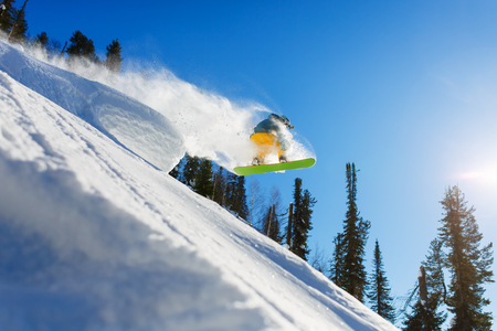 A snowboarder jumps from a springboard in the high mountains on a sunny day. Sun rays, white snow and clear weather, blue sky.の写真素材