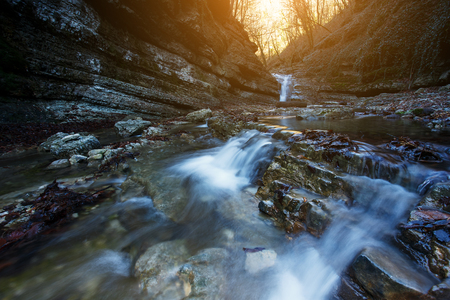 Beautiful waterfall at mountain river in colorful autumn forest with red and orange leaves at sunset. Nature landscape.の写真素材