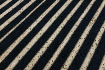 Sunlight shines through wooden fence and makes geometric stripes shadows on the ground. Shadows of wooden fence on the ground, Fence shadows textureの写真素材