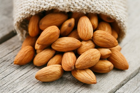 Almond nuts in a burlap bag on a wooden gray background.の写真素材