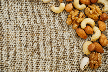 A mix of cashews, mendel, pistachios, hazelnuts and walnuts lies against a background of brown burlap fabric. Nuts as a texture and background, macroの写真素材