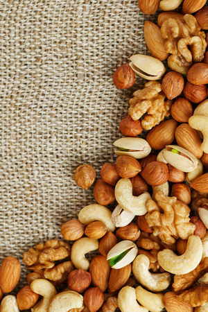 A mix of cashews, mendel, pistachios, hazelnuts and walnuts lies against a background of brown burlap fabric. Nuts as a texture and background, macro. Vertical frameの写真素材