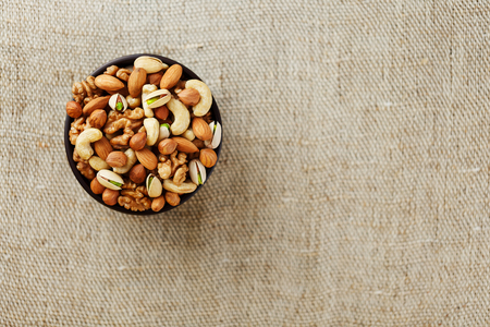 Mix of nuts of cashew, almonds, pistachios, hazelnuts and walnuts is against the background of brown fabric of burlap. Nuts as structure and background, macroの写真素材
