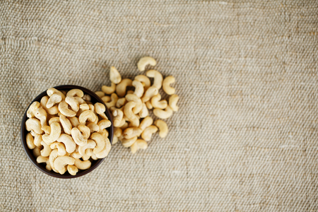 Cashew nuts in a wooden bowl on a burlap cloth background. Golden cashew close-up in a dark brown cup.の写真素材
