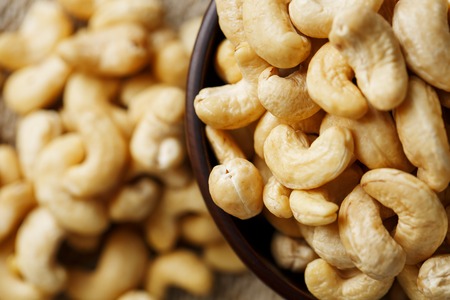 Cashew nuts in a wooden bowl on a burlap cloth background. Golden cashew close-up in a dark brown cup.の写真素材