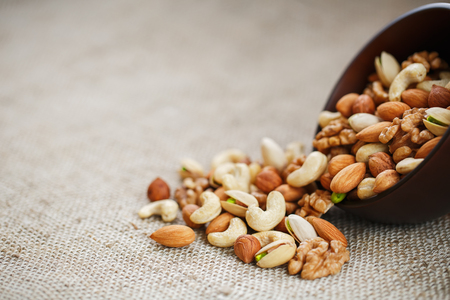 Mix of nuts of cashew, almonds, pistachios, hazelnuts and walnuts is against the background of brown fabric of burlap. Nuts as structure and background, macroの写真素材