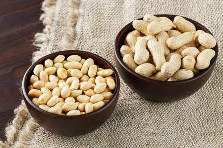 Peanuts in the shell and peeled close-up in cups. Roasted peanuts in their shells and peeled against...