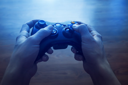Video game controller in the hands of man. In front of the TV in the evening, with blue light from...