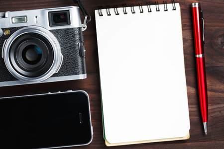 Classic camera with blank notepad page and red pen on dark brown wooden table, vintage table with...