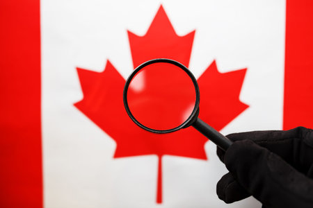 The flag of CANADA is looked through a magnifying glass. Espionage and surveillance of Canada. Monitoring the status of Kanatsev. The concept of the danger of theft of military terrorismの写真素材