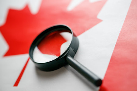 The flag of CANADA is looked through a magnifying glass. Espionage and surveillance of Canada. Monitoring the status of Kanatsev. The concept of the danger of theft of military terrorismの写真素材