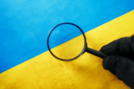 UKRAINE flag looking through a magnifying glass. Spying and monitoring Ukraine. Monitoring the state of the Ukrainian people. The concept of the danger of theft of military terrorismの写真素材