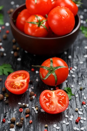Fresh Sliced Cherry Tomatoes on a black background with spices coarse salt and herbsの写真素材
