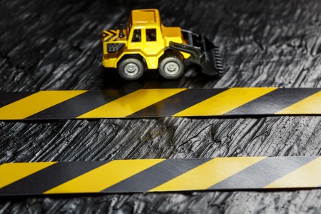 Toy excavator yellow on a black background texture. Tape fence black and yellow on the background. CONCEPT. Business, repair, services.の写真素材