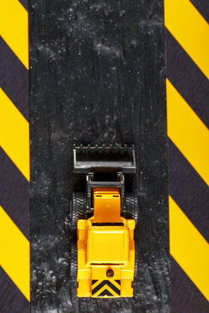 Yellow toy bulldozer on a black background texture. Black and yellow fence tape against the...