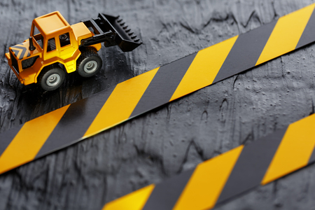 Yellow toy bulldozer on a black background texture. Black and yellow fence tape against the background of the CONCEPT. Business, repair, services.の写真素材