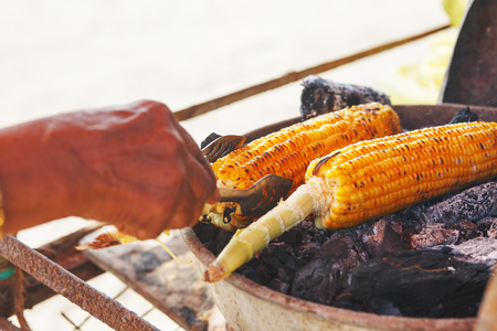 Corn cobs on the grill. Close-up image with corns and hands. Asian, Indian and Chinese street food. Trolley on the beach GOA.の写真素材