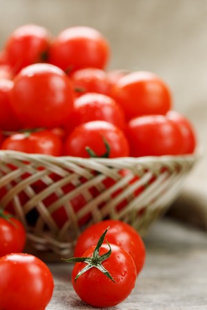 Ripe and juicy cherry tomatoes with drops of moisture in a wicker basket. Old wooden table, around the canvas of burlap. Country style.の写真素材