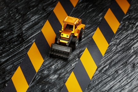 Yellow toy bulldozer on a black background texture. Black and yellow fence tape against the background of the CONCEPT. Business, repair, services.の写真素材